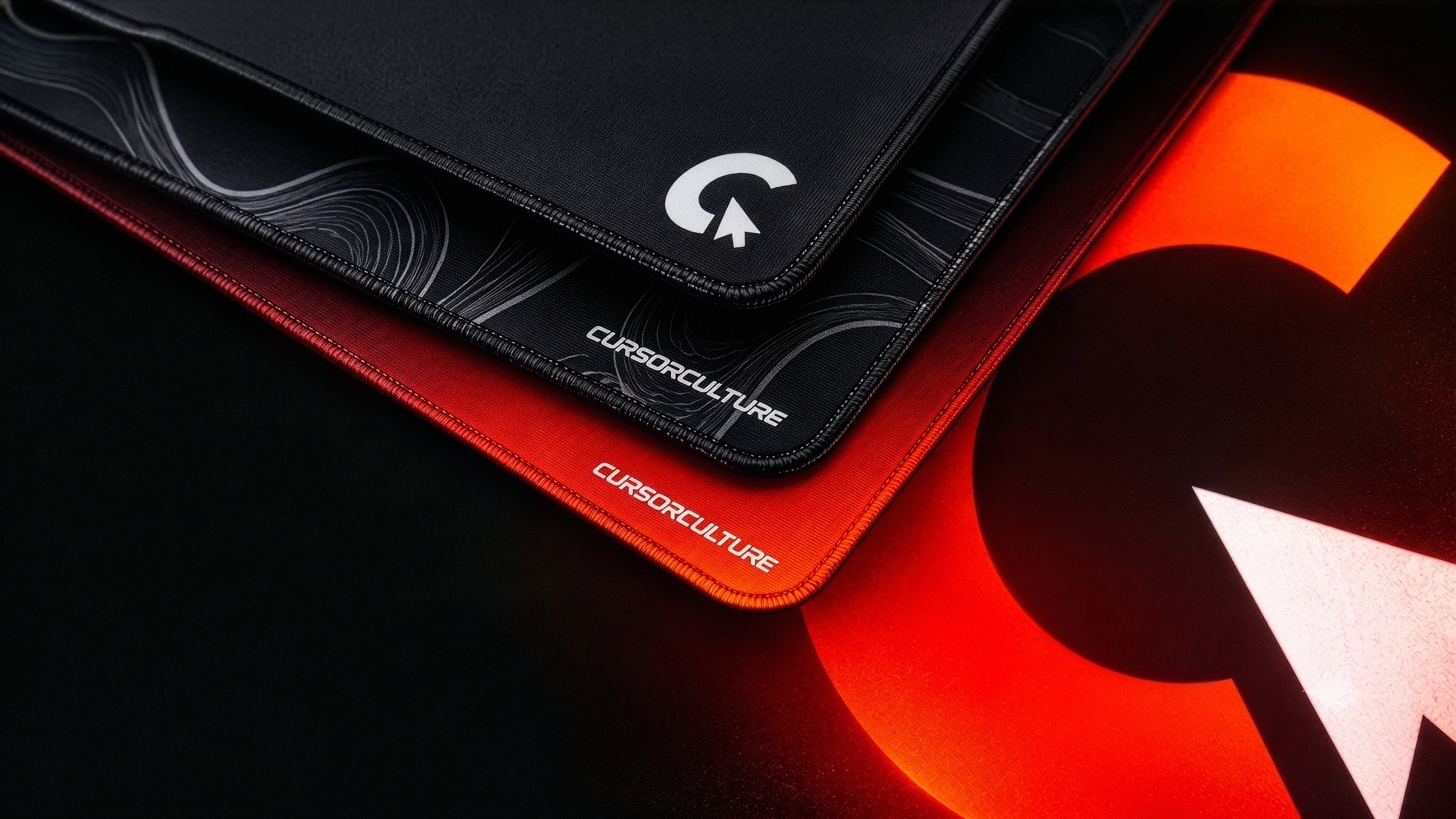 Stacked premium CursorCulture custom mousepads in black and red-orange with a glowing cursor graphic
